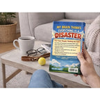 Person holding a book titled 'My Brain Thinks Everything is a Disaster' on a coffee table with a cup of coffee and glasses.